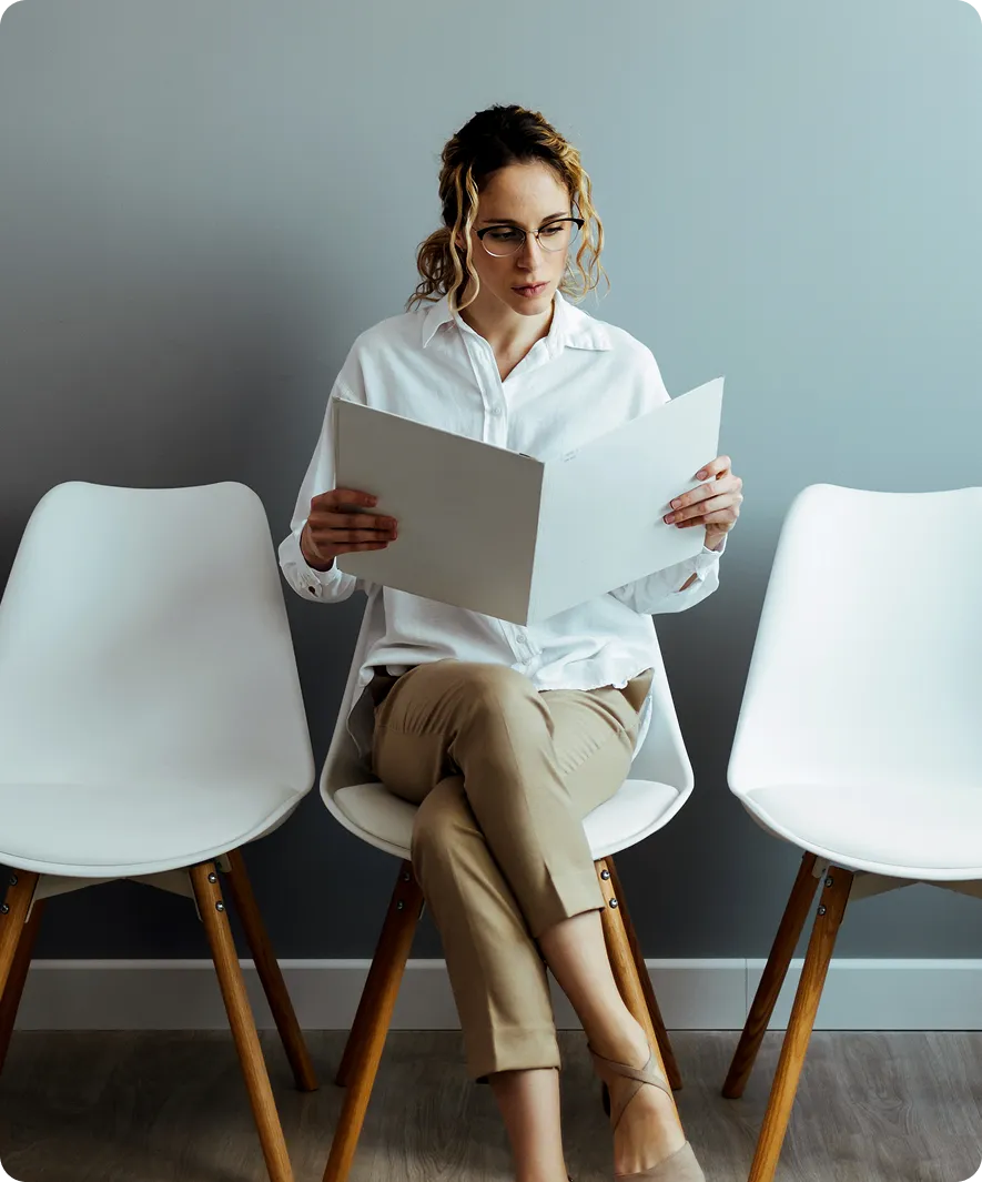 Woman reading a document between chairs.